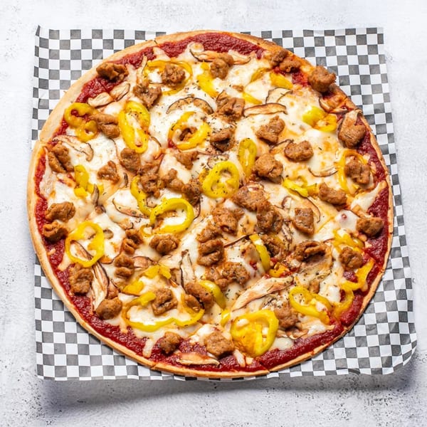 A whole pizza with sausage, yellow peppers, and mushrooms on a checkered paper.