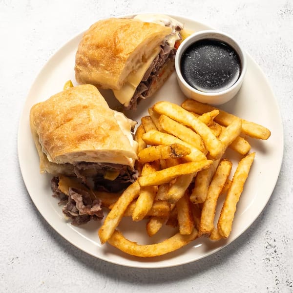 Two halves of a French dip sandwich with fries and a side of au jus on a white plate.