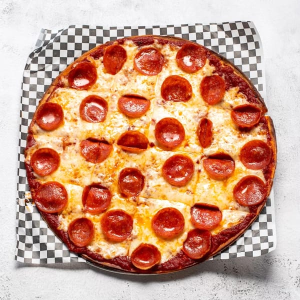 A whole pepperoni pizza with melted cheese and a thick crust, on checkered paper.