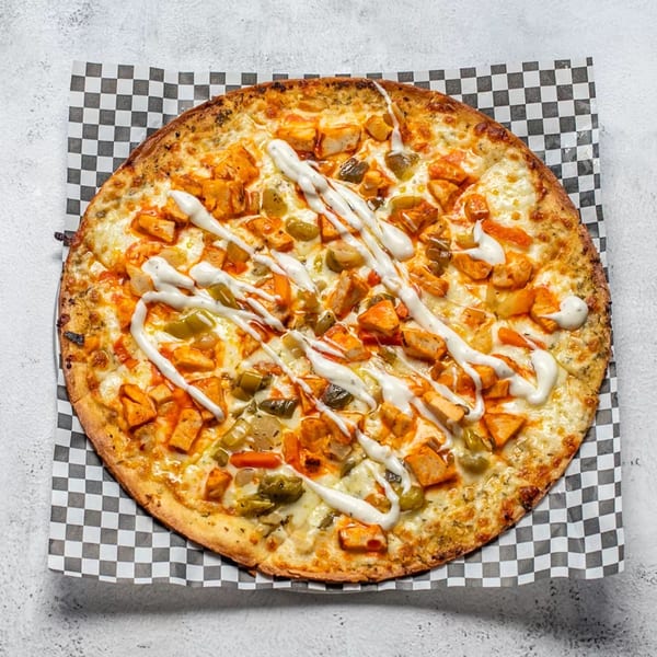 Overhead view of a buffalo chicken pizza with ranch drizzle on checkered paper.